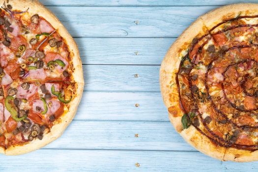 Two different delicious big pizzas on a blue wooden background.