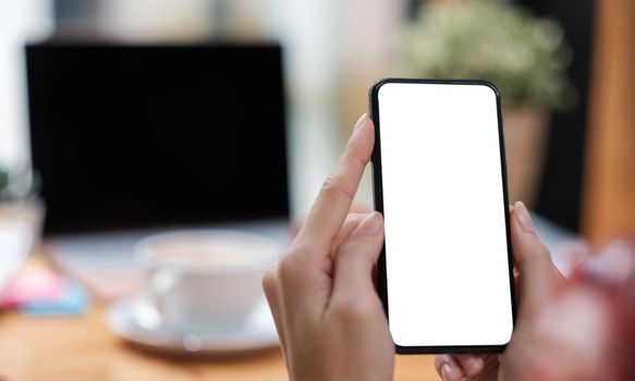 Mockup image blank white screen cell phone.women hand holding texting using mobile on desk at home office..