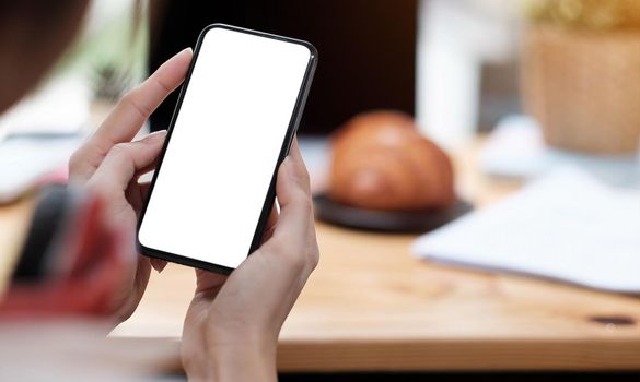 Mockup image blank white screen cell phone.women hand holding texting using mobile on desk at home office..