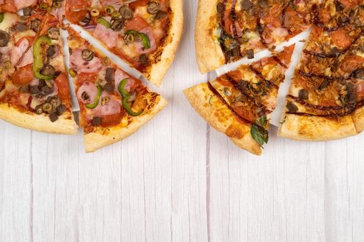 Two different delicious large pizzas on a light wooden background.