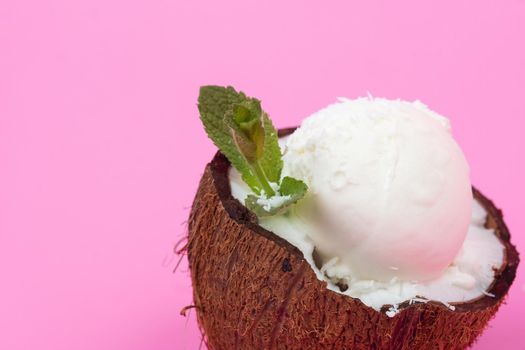 Vanilla ice cream balls in fresh coconut halves, decorated with mint leaves on a pink background.