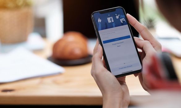 CHIANG MAI ,THAILAND AUG 18 2020 : Woman holding a iPhone X with social Internet service Facebook on the screen..