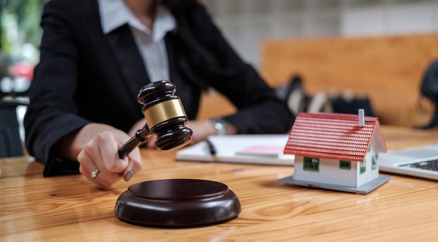 Real Estate Law concept. Gavel on sounding block in hand's female judge at a courtroom, working for the insurance compensations. report the case on table