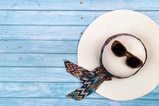 Top view of a straw white hat with glasses lying on a blue wooden background.Summer vacation concept.
