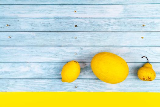 An assortment of yellow fruits lies on a blue wooden background and a yellow background.
