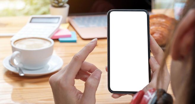 Mockup image blank white screen cell phone.women hand holding texting using mobile on desk at home office..