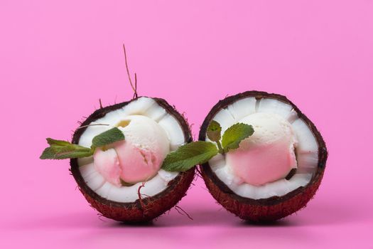 Vanilla ice cream balls in fresh coconut halves decorated with mint leaves on a pink background.