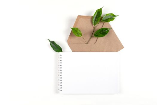 Notepad and an envelope made from recycled paper lie on white surface with sprig of a green plant. Ecology concept, recyclable, no waste, office, business. Selective focus. Copy space.
