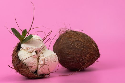 Vanilla ice cream balls in an empty coconut decorated with mint leaves on a pink background.