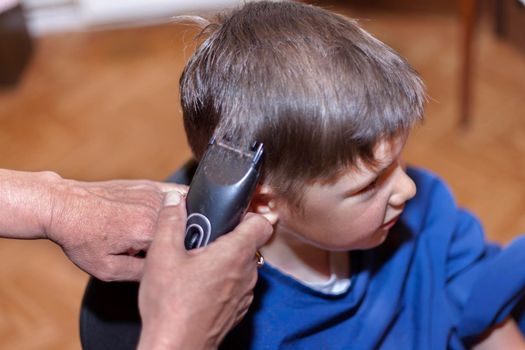 Boy is having a home haircut with a hair trimmer in home. living at home during lockdown.