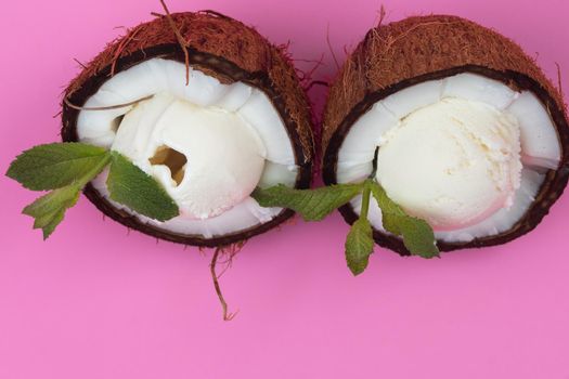 Vanilla ice cream balls in fresh coconut halves decorated with mint leaves on a pink background.