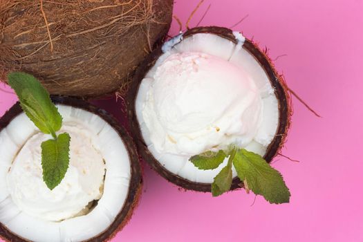 Vanilla ice cream balls in fresh coconut halves decorated with mint leaves on a pink background.