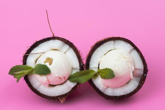 Vanilla ice cream balls in fresh coconut halves decorated with mint leaves on a pink background.