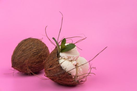 Vanilla ice cream balls in an empty coconut decorated with mint leaves on a pink background.