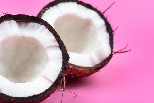 Two halves of a ripe coconut with white flesh on a pink background..
