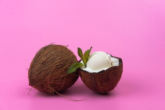 Vanilla ice cream balls in fresh coconut halves decorated with mint leaves on a pink background.