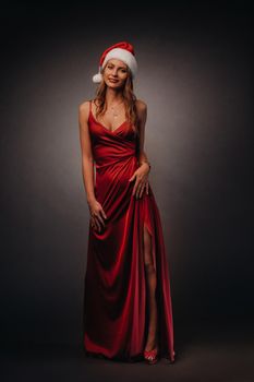 a woman in a red long dress and a Christmas hat on a black background.A smiling girl in a new year direction on a dark background.