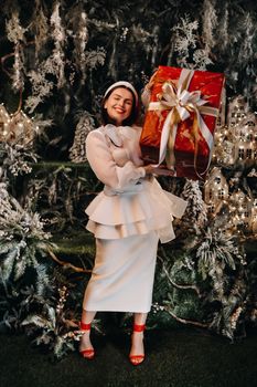 a girl in a Santa hat with a big Christmas gift in her hands on a fairy-tale island.Smiling woman in white clothes on the background of Christmas trees and small houses.