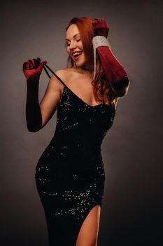 Red-haired girl in a black dress and elegant gloves on a black background.