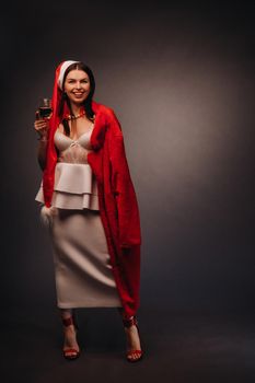 a woman in a Christmas hat and white dress, holding a glass and a red fur coat in her hands, on a black background, Christmas, holiday,