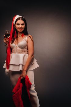 a woman in a Christmas hat and white dress, holding a glass and a red fur coat in her hands, on a black background, Christmas, holiday,