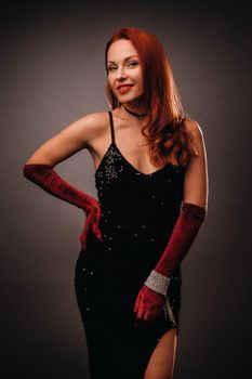 Red-haired girl in a black dress and elegant gloves on a black background.