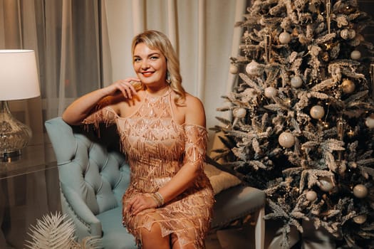 A girl in an evening dress is sitting on the sofa near the Christmas tree.