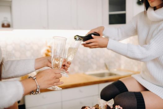 two girls in a cozy home environment in the kitchen pour champagne for Christmas. Smiling girls drink champagne on a festive evening.