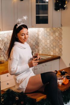 A girl on Christmas day is sitting on the kitchen table and holding a glass of champagne.Woman on new year's eve with champagne.