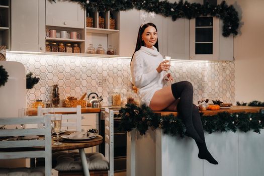 A girl on Christmas day is sitting on the kitchen table and holding a glass of champagne.Woman on new year's eve with champagne.