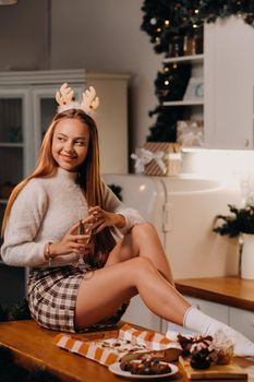 A girl on Christmas day sits on the kitchen table and holds a glass of champagne in her hands.A woman on New year's eve in the kitchen with champagne.