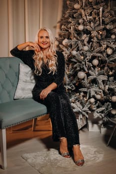 A girl in an evening dress is sitting on the sofa near the Christmas tree.