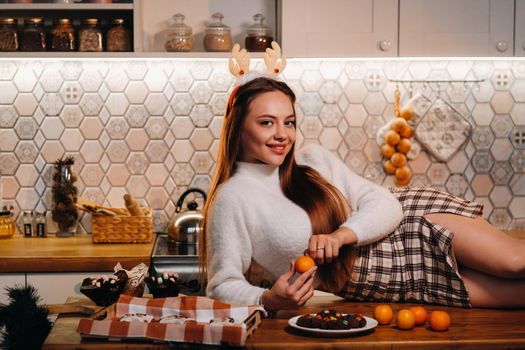 A girl at Christmas is lying on the kitchen table and holding a tangerine in her hands.Woman on new year's eve in the kitchen lying with horns.