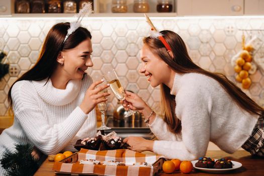 two girls in a cozy home environment with champagne in their hands at Christmas. Smiling girls drink champagne on a festive evening.