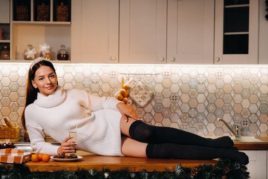 A girl at Christmas is lying on the kitchen table and holding a glass of champagne.Woman on new year's eve with champagne.