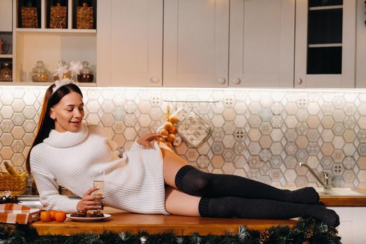 A girl at Christmas is lying on the kitchen table and holding a glass of champagne.Woman on new year's eve with champagne.