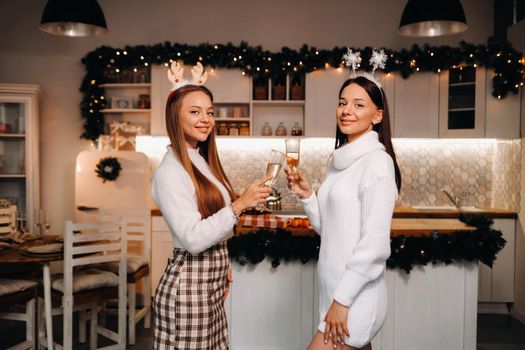 two girls in a cozy home environment with champagne in their hands at Christmas. Smiling girls drink champagne on a festive evening.