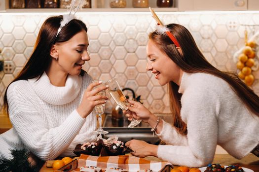 two girls in a cozy home environment with champagne in their hands at Christmas. Smiling girls drink champagne on a festive evening.