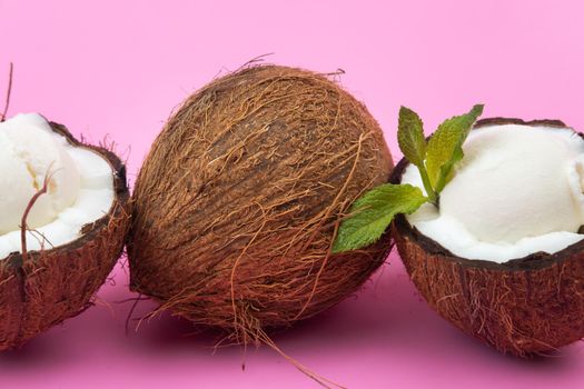 Vanilla ice cream balls in fresh coconut halves decorated with mint leaves on a pink background.