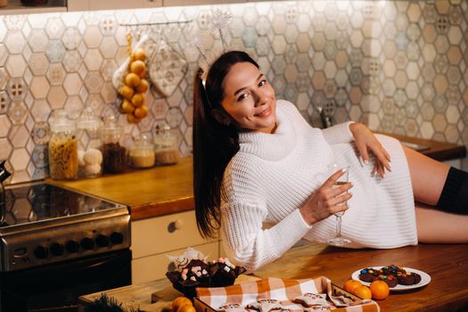 A girl at Christmas is lying on the kitchen table and holding a glass of champagne.Woman on new year's eve with champagne.