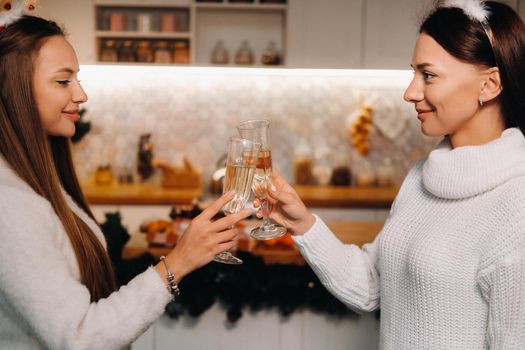 two girls in a cozy home environment with champagne in their hands at Christmas. Smiling girls drink champagne on a festive evening.