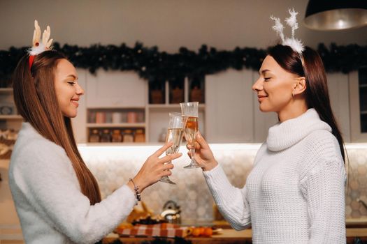 two girls in a cozy home environment with champagne in their hands at Christmas. Smiling girls drink champagne on a festive evening.