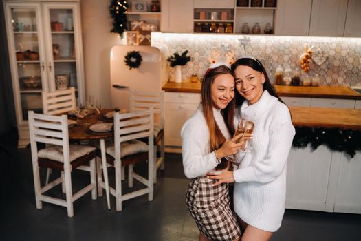 two girls in a cozy home environment with champagne in their hands at Christmas. Smiling girls drink champagne on a festive evening.