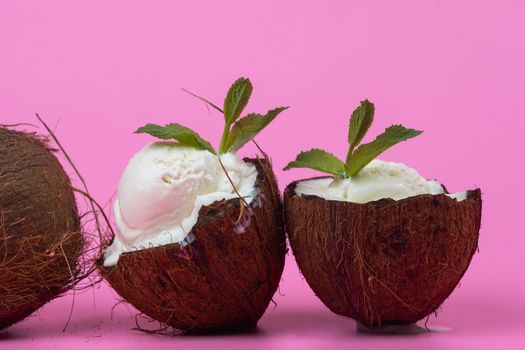 Vanilla ice cream balls in fresh coconut halves decorated with mint leaves on a pink background.