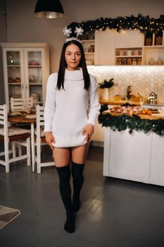 Girl at Christmas with horns in the home interior.A woman on New year's eve in a white sweater.