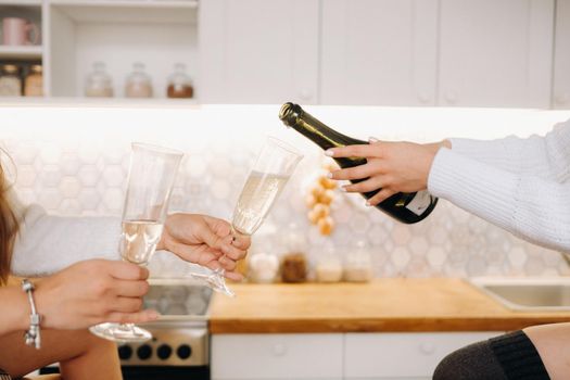 two girls in a cozy home environment in the kitchen pour champagne for Christmas. Smiling girls drink champagne on a festive evening.