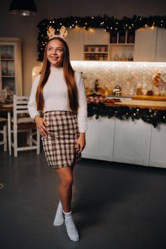 Girl for Christmas with reindeer horns in the home interior.A woman on New year's eve in a white sweater and skirt.