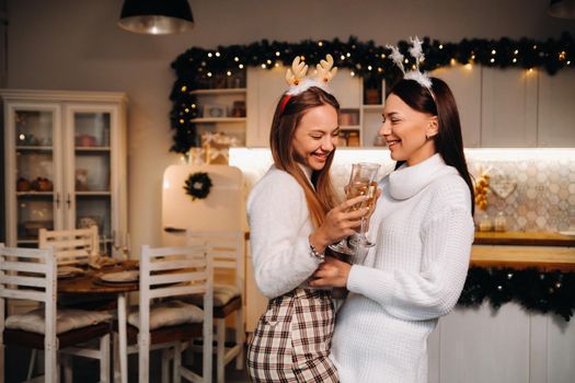 two girls in a cozy home environment with champagne in their hands at Christmas. Smiling girls drink champagne on a festive evening.