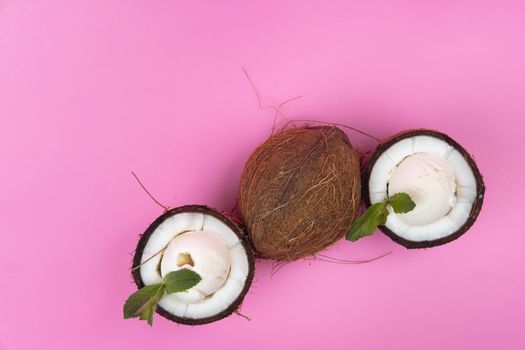 Vanilla ice cream balls in fresh coconut halves decorated with mint leaves on a pink background.
