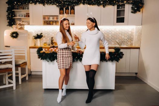 two girls in a cozy home environment with champagne in their hands at Christmas. Smiling girls drink champagne on a festive evening.